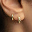A close-up view of a person's ear, showing two gold hoop earrings.