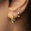 A close-up view of a person's ear, showing two gold hoop earrings.