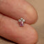 A close-up image of a person's finger holding a small, delicate piece of jewelry, which appears to be a small, intricately designed earring.