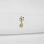 A gold-colored earring with a star-shaped design and a small flower-like charm hanging from it, placed on a white fabric surface.