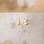 A pair of gold-colored earrings in the shape of small cats, placed on a white surface.