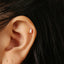 A close-up view of a person's ear with a small, gold-colored earring inserted into the earlobe.