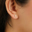 A close-up view of a person's ear with a small, rectangular earring featuring a white stone or gemstone.