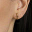 A close-up of a person's ear wearing a gold-colored earring shaped like a sword.