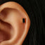 A close-up view of a person's ear with a small, square-shaped earring in the earlobe.