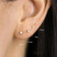 A close-up of a person's ear with four small earrings, each with a small opal stone, and the sizes of the earrings are indicated in millimeters.