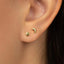 A close-up view of a person's ear with two small gold earrings, one shaped like a star and the other like a crescent moon.