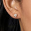 A close-up of a person's ear wearing a small, delicate earring with a flower-shaped design and white stones.
