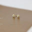 A pair of gold earrings with white stones, resting on a brown surface.