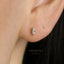 A close-up of a person's ear with a small, delicate earring featuring a single diamond.