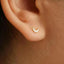 A close-up view of a person's ear with a small, delicate earring featuring a crescent moon design.