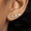 A close-up of a person's ear with three small diamond earrings.