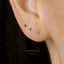 A close-up of a person's ear with three small earrings with gemstones in different colors.