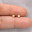 A close-up image of a person's fingers holding a pair of small gold earrings with small diamonds.