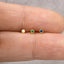 A close-up image of three small gold-colored earrings with gemstones, placed on a person's fingers.