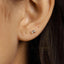 A close-up of a person's ear with a small gold earring featuring a rectangular gemstone.