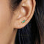 A close-up of a person's ear with a small earring featuring green gemstones.