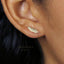 A close-up view of a person's ear with a small gold feather earring attached.