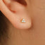 A close-up view of a person's ear with a small gold-colored earring featuring a triangular design and small diamonds.