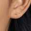 A close-up view of a person's ear with a small gold-colored earring inserted.