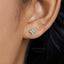 A close-up of a person's ear wearing a small turquoise-colored earring with a small flower-shaped accent.
