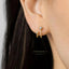 A close-up view of a person's ear adorned with a pair of gold earrings featuring small diamonds.