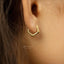 A close-up view of a person's ear with a gold-colored hexagonal earring.