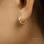 A close-up view of a person's ear, showing a gold-colored earring with a hexagonal shape.