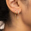 A close-up view of a person's ear adorned with a pair of gold earrings featuring a chain and small diamonds.