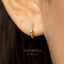 A close-up view of a person's ear adorned with a gold hoop earring featuring a small gemstone.