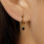 A close-up view of a person's ear, showing a gold hoop earring with a black gemstone hanging from it.