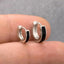 A close-up image of a person's fingers holding two small silver earrings with black stones.