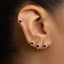 A close-up view of a person's ear adorned with three gold earrings, each featuring a blue gemstone.