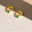 A pair of gold earrings with green gemstones, placed on a textured surface.
