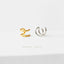 two earrings, one gold and one silver, placed side by side on a white background.