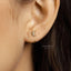 A close-up view of a person's ear with a small gold earring featuring a crescent moon design.