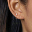 A close-up of a person's ear with a small hoop earring and a small opal stone in the earlobe.