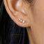 A close-up view of a person's ear adorned with a delicate gold earring featuring three small stones.