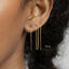 A close-up of a person's ear wearing three gold-colored dangling earrings.