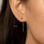 A close-up of a person's ear with a green gemstone earring and a dangling gold chain.
