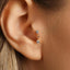 A close-up view of a person's ear adorned with a delicate gold earring featuring a single diamond.