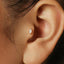 A close-up view of a person's ear, showing a small, delicate earring with a small, round stone or gemstone in the center.