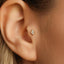 A close-up of a person's ear with a small gold earring featuring a diamond-like stone in the earlobe.