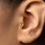 A close-up view of a person's ear, showing a small gold-colored earring with a flower-like design.
