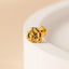 A close-up image of a gold-colored flower-shaped earring resting on a white surface.