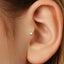 A close-up view of a person's ear, showing a small gold-colored earring or stud inserted into the earlobe.