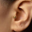 A close-up of a person's ear with a small gold-colored earring shaped like a snail or similar creature.