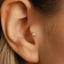 A close-up view of a person's ear, showing a small gold-colored earring with a diamond-like stone in the center.
