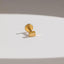 A small gold-colored metal object, possibly a pin or earring, is resting on a white surface.