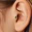 A close-up view of a person's ear, showing a small green gemstone or earring inserted into the earlobe.